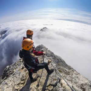 Couple climbing via ferrata, a secure climbing route found in Alps. Alpine climbing on a sunny day in the mountains. Valley covered in fog, temperature inversion in the valley.